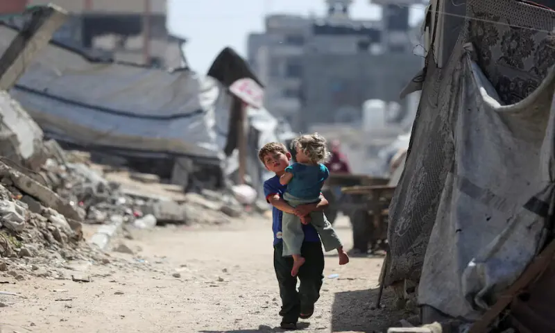 A Palestinian boy, carrying a child, walks through an area damaged by Israeli strikes in Gaza City. -- Reuters