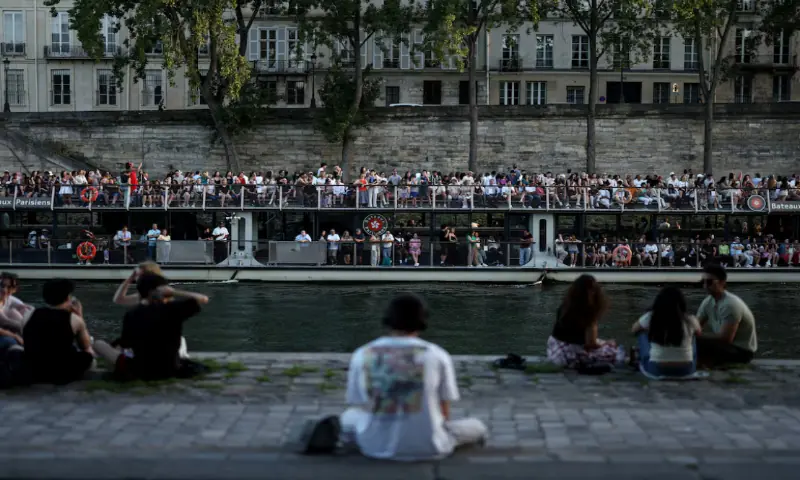 A boat passes people sitting on the banks of the Seine River, as temperatures reached up to 35 degrees during a period of hot weather in Paris, France. -- Reuters