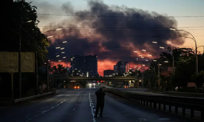 A man takes a picture of a street as smoke rises in the background after an overnight Russian missile and drone strike in Kyiv, Ukraine, on Tuesday. -- Reuters