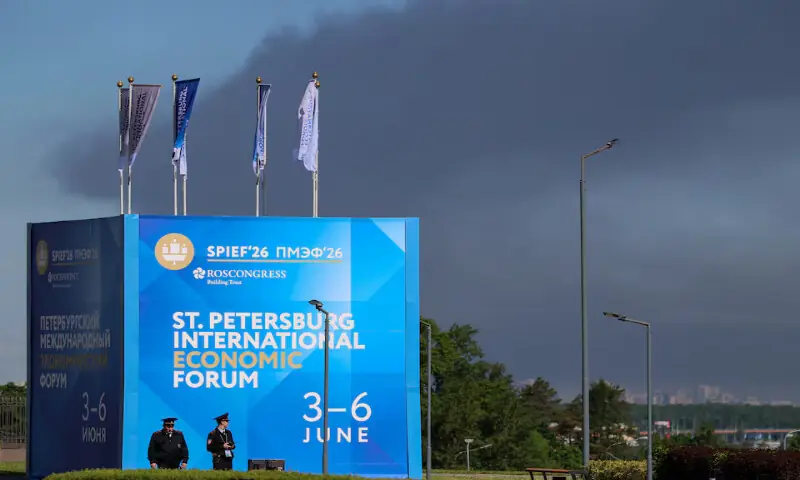 Police officers stand in front of a banner and flags with the logo of the St. Petersburg International Economic Forum as heavy smoke billows in the background after drones hit infrastructure in St Petersburg, Russia, on Wednesday. -- Reuters