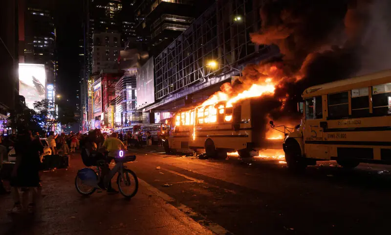 Revellers and fans celebrating the New York Knicks&rsquo; victory over the San Antonio Spurs stand near a shuttle bus set fire outside the Port Authority Bus Terminal in New York City, US. -- Reuters