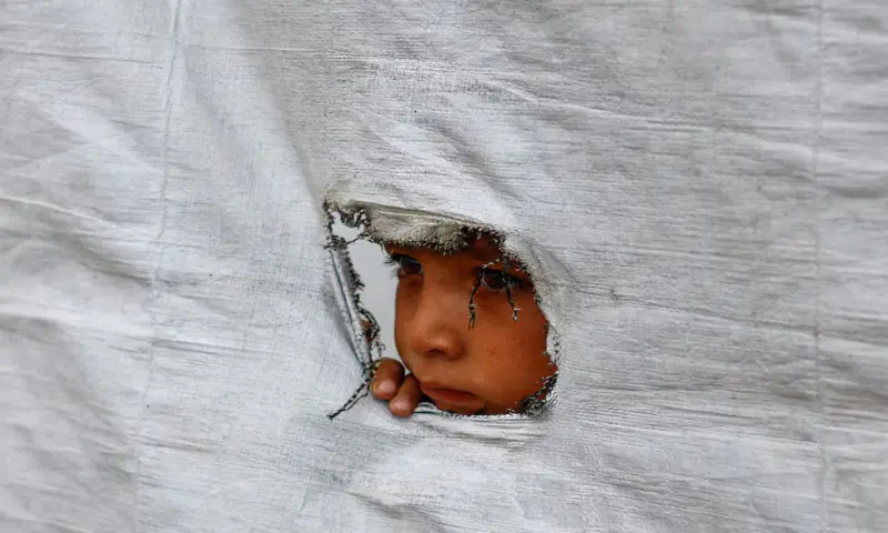 A displaced Palestinian boy peers through a tear in a tent wall, in Gaza City. -- Reuters