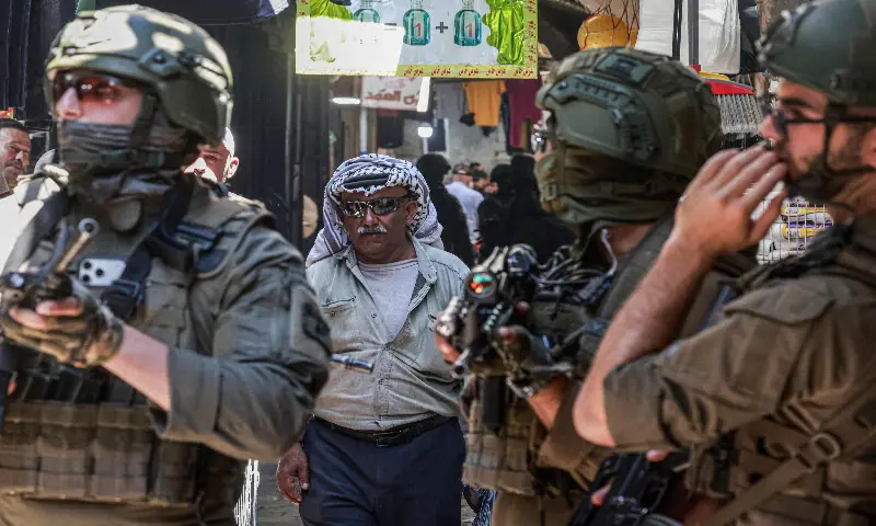 A Palestinian man walks past Israeli soldier patrolling the market in the Old City of Nablus in the northern Israeli-occupied West Bank on June 23, 2026. AFP