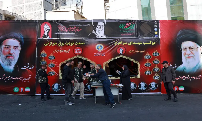 A volunteer hands out refreshments in front of portraits of Iran's supreme leader Ayatollah Mojtaba Khamenei (left) and slain supreme leader Ayatollah Ali Khamenei (right) while mourners make their way to the Grand Mosalla to pay their final respects at the start of his funeral ceremonies in Tehran on July 4, 2026. AFP A volunteer hands out refreshments in front of portraits of Iran's supreme leader Ayatollah Mojtaba Khamenei (left) and slain supreme leader Ayatollah Ali Khamenei (right) while mourners make their way to the Grand Mosalla to pay their final respects at the start of his funeral ceremonies in Tehran on July 4, 2026. AFP