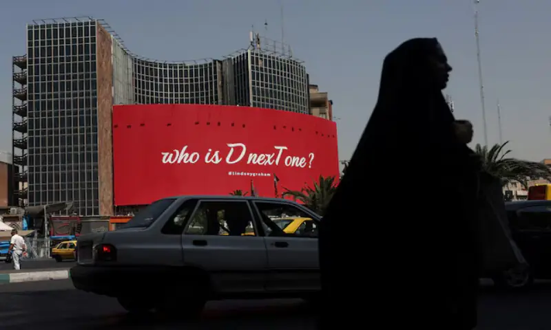 A woman walks near a billboard with a slogan referring to US President Donald Trump and a hashtag referring to late US Senator Lindsay Graham, in Tehran, Iran. -- Reuters