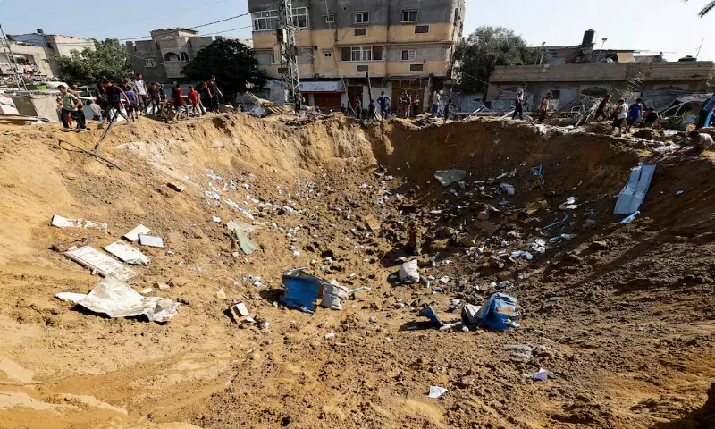 Palestinians stand by a crater after an Israeli strike on a medicine warehouse in Deir Al Balah in the central Gaza Strip. -- Reuters Palestinians stand by a crater after an Israeli strike on a medicine warehouse in Deir Al Balah in the central Gaza Strip. -- Reuters