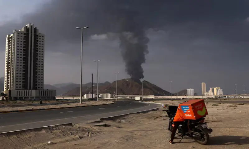 A person stands next to a motorcycle as smoke rises following an alleged drone strike in Fujairah, United Arab Emirates. -- Reuters file