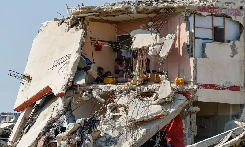 Palestinians sit inside a house damaged in an Israeli strike, surrounded by destroyed buildings, in Gaza City. -- Reuters